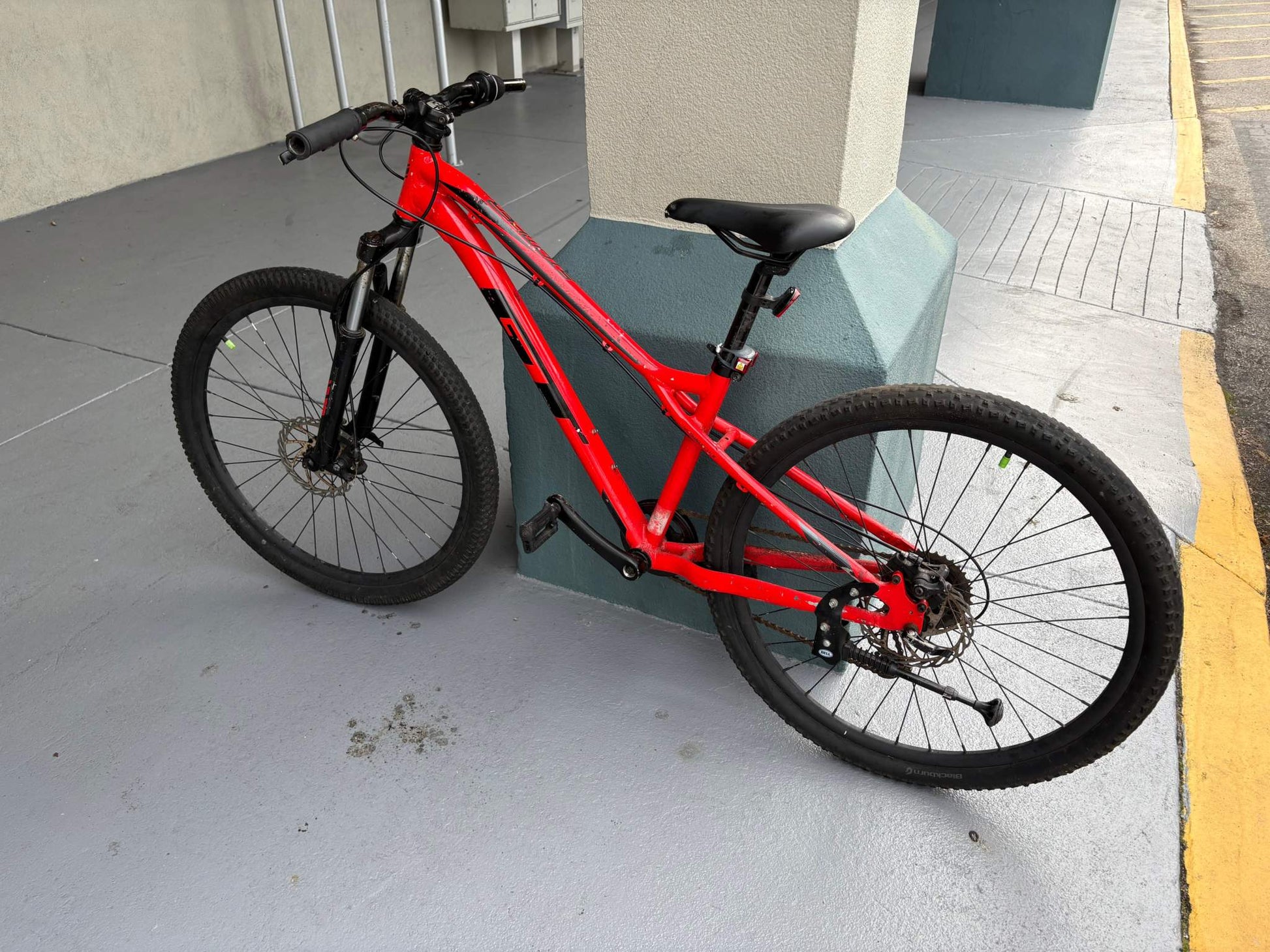 Red mountain bike for rent leaning against a pillar, available for hourly, daily, and monthly rental.