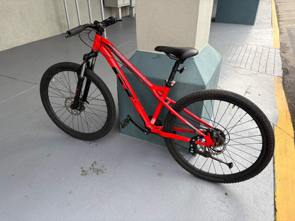Red mountain bike for rent leaning against a pillar, available for hourly, daily, and monthly rental.